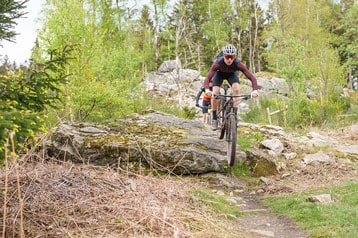 Fietser rijdt over rotsachtig terrein in een bos met bomen en struiken.