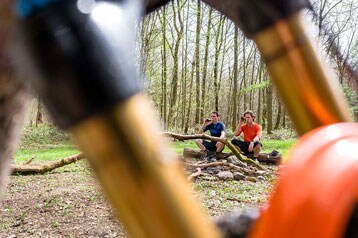 Twee personen zitten in een open plek in het bos, omlijst door fietsonderdelen.