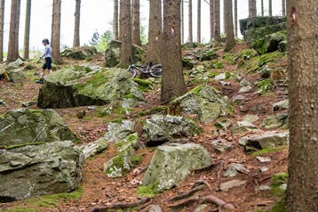 Fietser loopt met een mountainbike over een rotsachtig bospad.