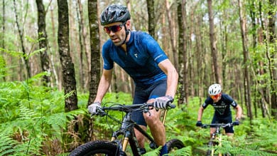 Twee fietsers rijden op mountainbikes over een bospad.