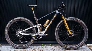 Mountainbike met Shimano-onderdelen en Maxxis-banden geparkeerd tegen een donkere muur.