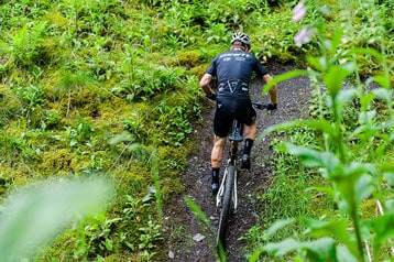 Fietser rijdt bergopwaarts op een bospad omgeven door groen.