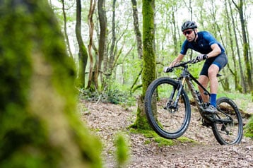 Mountainbiker springt over een pad in het bos.