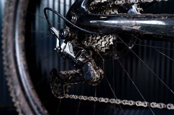 Close-up van een modderige fietsketting en tandwielen.
