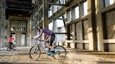 Twee fietsers rijden in een industrieel gebouw met stoffige vloer.