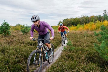 Twee fietsers op een pad tussen groene en herfstkleurige bladeren.
