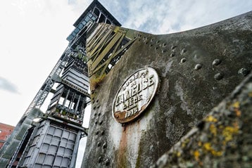 Industrieel bouwwerk met verweerde metalen plaquette en bewolkte hemel op de achtergrond.
