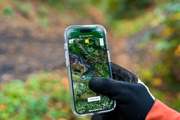 Persoon gebruikt een mountainbikekaart-app op een smartphone in de buitenlucht.
