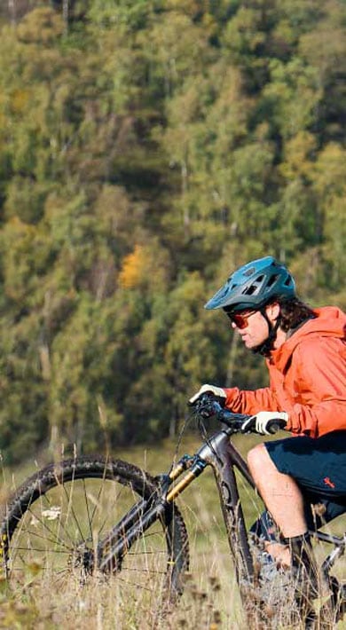 Fietser rijdt op een grasheuvel met bos op de achtergrond.