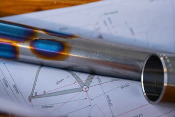 Metal pipe with heat coloration resting on technical drawings