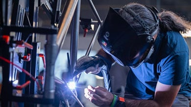 Man welding metal in a workshop with protective gear and helmet