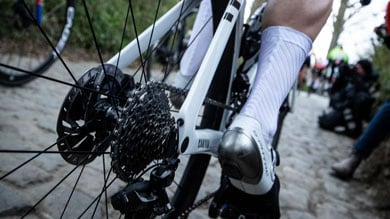 Wielrenner rijdt op een kasseienpad met de focus op het achterwiel van de fiets.