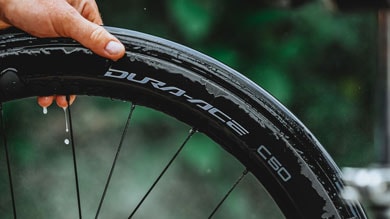 Hand houdt een natte fietsband vast met Dura-Ace C50-branding.