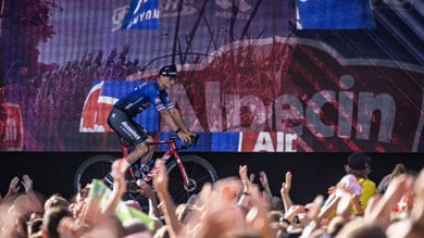 Wielrenner in een blauw shirt rijdt langs een juichende menigte en kleurrijke banners.