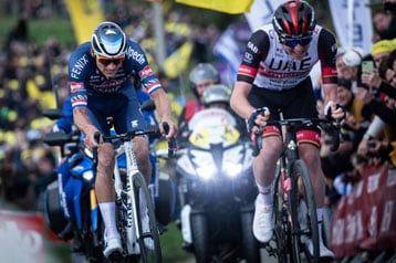 Twee wielrenners racen, dicht gevolgd door motorfietsen.
