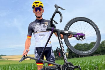 Michael Teuber hält sein Fahrrad in einem schwarz-weißen Trikot hoch.