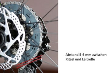 Nahaufnahme eines Fahrradrades mit einem 5-6 mm Abstand zwischen dem Ritzel und der Führungsrolle, mit Speichen, Felge und Reifen aus synthetischem Gummi.