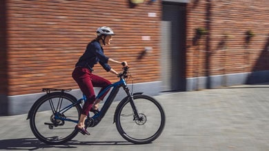 Person riding a blue electric bicycle on a city street, wearing a white helmet and casual attire