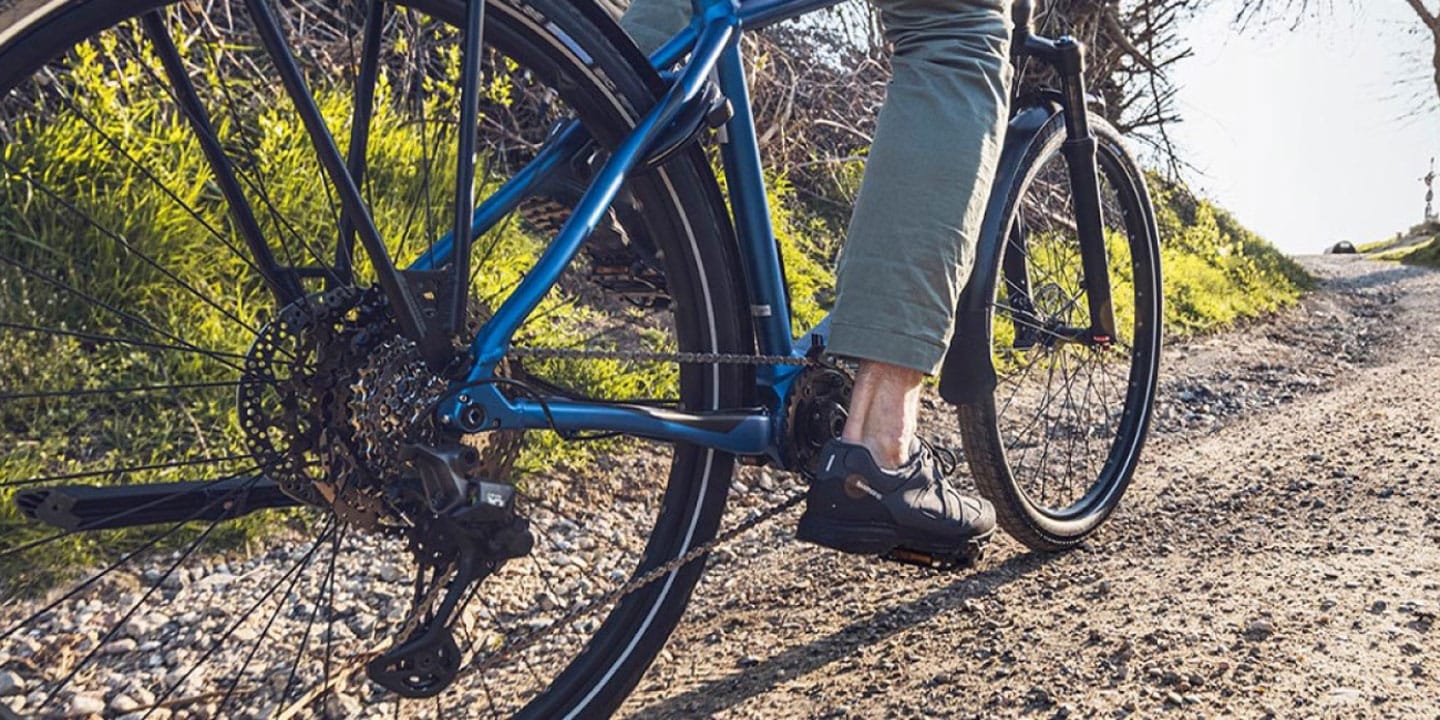 Person riding a bicycle on a gravel road surrounded by greenery