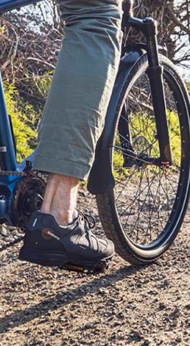 Person riding a bicycle on a gravel road surrounded by greenery