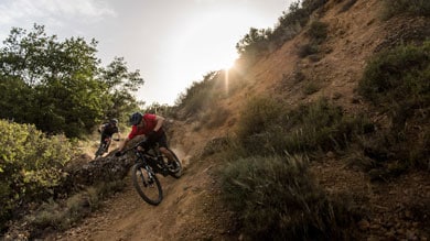 Two mountain bikers ride down a rugged trail during sunset