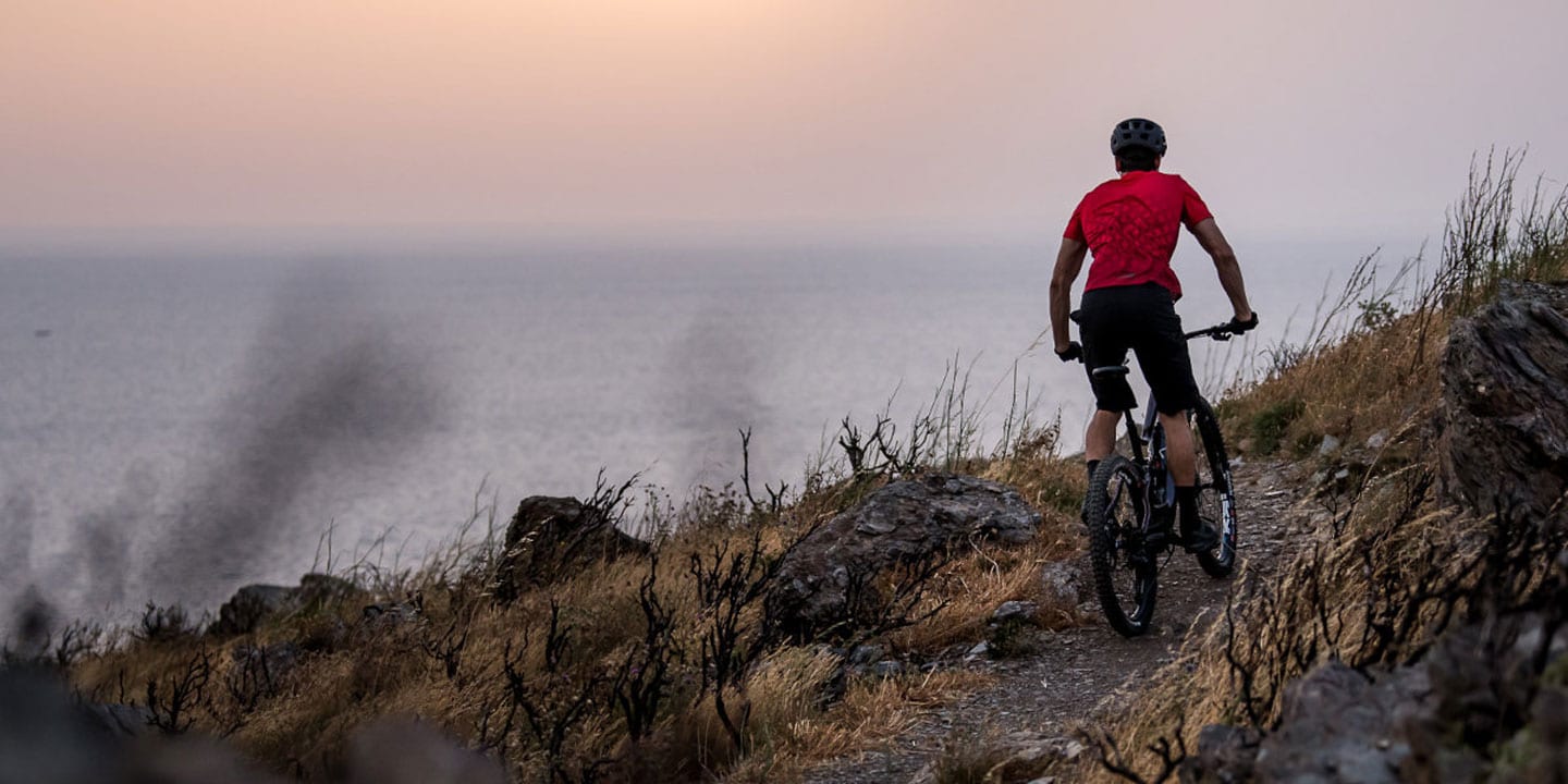 Cyclist riding a mountain trail by the ocean at sunset