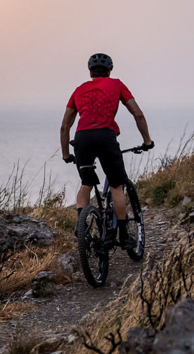 Cyclist riding a mountain trail by the ocean at sunset