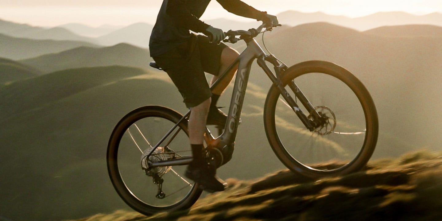 Cyclist riding a mountain bike on a trail with a scenic mountain backdrop