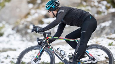 Cyclist wearing black attire and helmet riding a bike on a snowy path