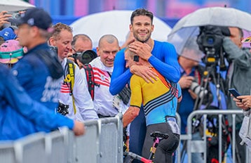 Deux athlètes s'embrassent après une course, entourés de photographes et de spectateurs.