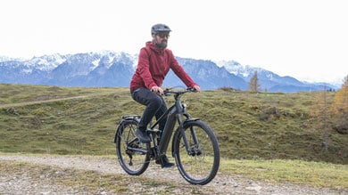 Person fährt mit einem Fahrrad auf einem Bergpfad mit schneebedeckten Gipfeln im Hintergrund.
