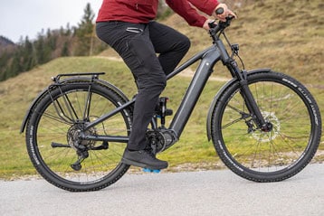 Person fährt ein schwarzes E-Bike auf einer landschaftlich schönen Straße.