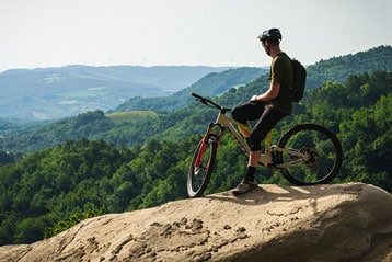 Cyclist on a mountain bike pausing atop a hill with scenic green landscape in the background.