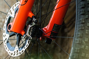 Close-up of a mountain bike's front disc brake and orange suspension fork.