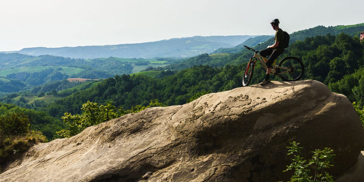 Cyclist on a rocky hilltop overlooking a green landscape