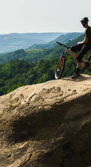 Cyclist on a rocky hilltop overlooking a green landscape