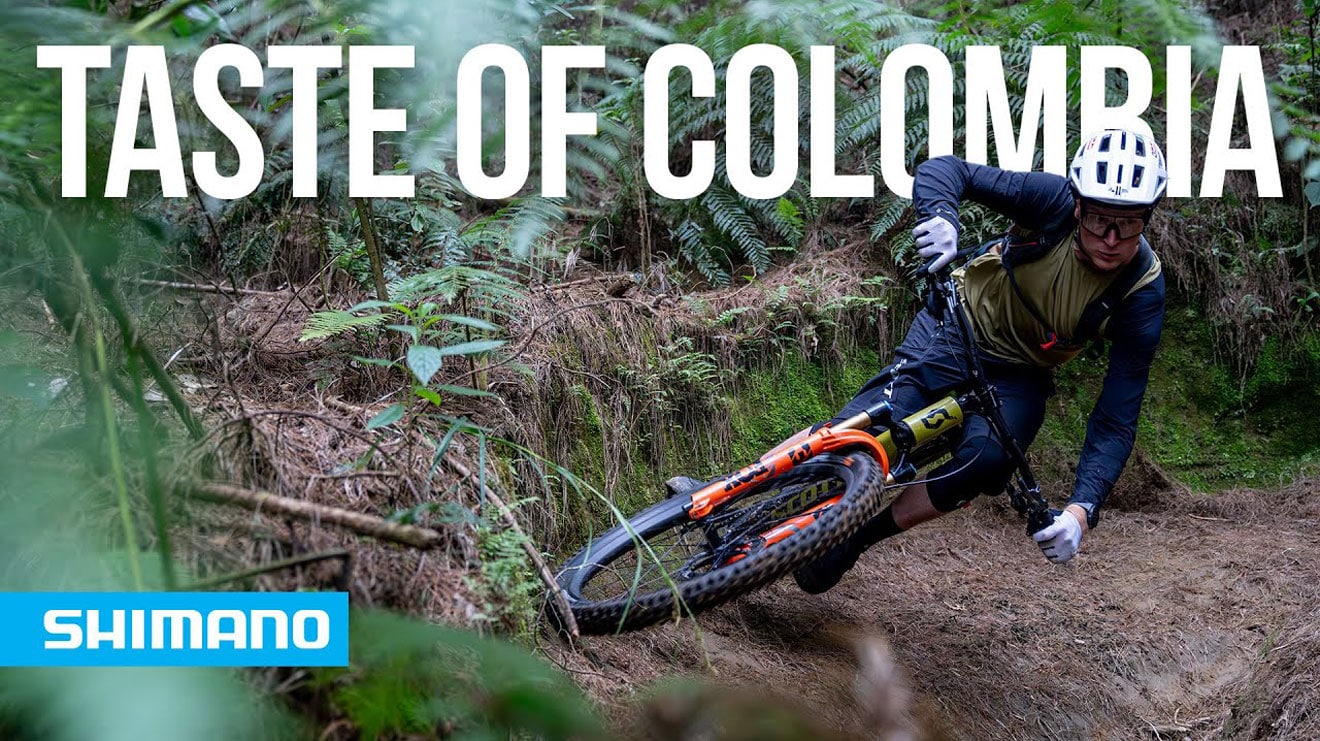 Mountain biker navigating a forest trail with 'Taste of Colombia' text