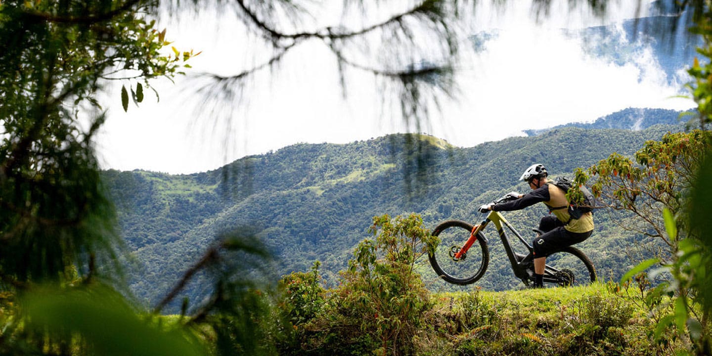 Mountain biker riding on a trail with lush green hills in the background