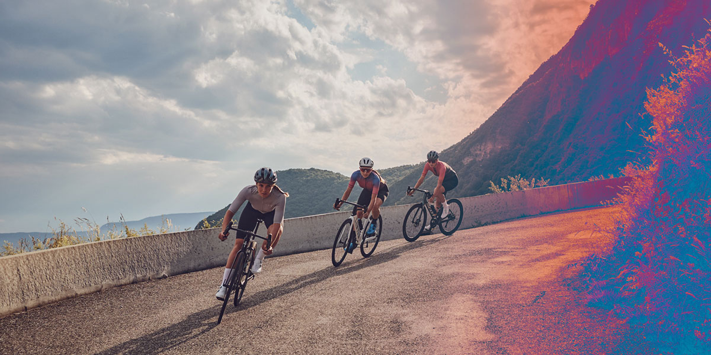 Three cyclists riding on a mountain road during a cloudy day