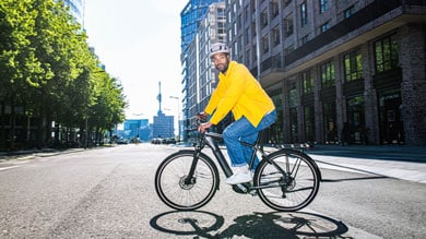 Man in yellow jacket and helmet riding a bicycle on a city street