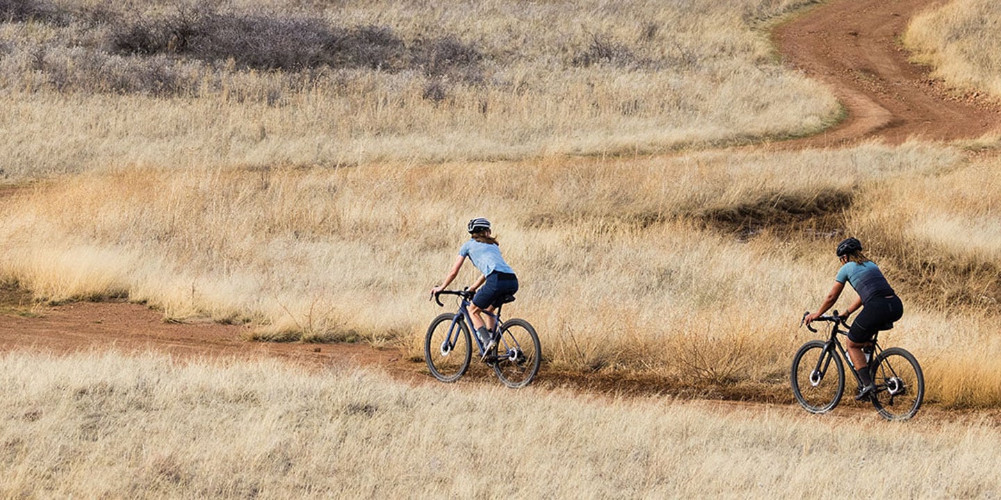 Two cyclists riding on a winding dirt path through dry grasslands