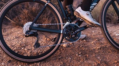 Nahaufnahme des Antriebs eines Gravelbikes mit Shimano GRX-Kurbelgarnitur, Kette und Schaltwerk. Der Schuh des Fahrers ist im Pedal eingeklickt.