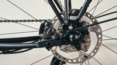 Nahaufnahme des hinteren Scheibenbremssystems eines Fahrrads, mit Shimano GRX-Bremssattel und einer großen, belüfteten Bremsscheibe. Der schwarze Rahmen und die Speichen kontrastieren mit den metallischen Komponenten.