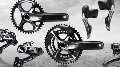 Eine Shimano GRX-Schaltgruppe mit Kurbeln, Schaltwerken und Schalthebeln vor einem rauen Offroad-Hintergrund.
