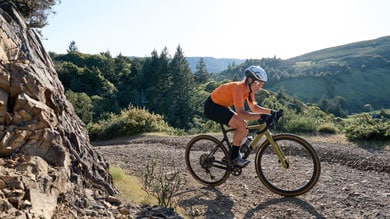 Cyclist in an orange jersey riding a gravel bike on a scenic trail