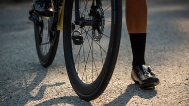 Cyclist's shoe next to a bicycle wheel on an asphalt road