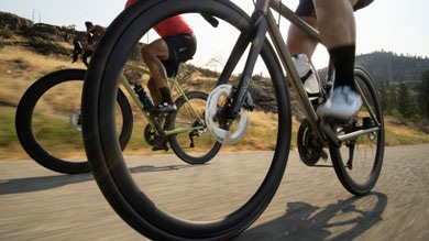 Close-up of two cyclists riding on a road with mountains in the background