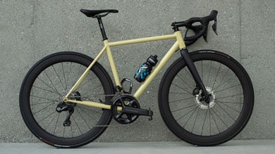 Yellow road bike with black components and water bottle, leaning against a concrete wall