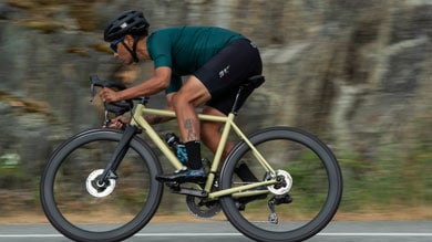 Cyclist in helmet and sunglasses riding a bike on a road with a rocky background