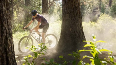 Fietser die over een mistig bospad fietst, zonlicht filtert door de bomen